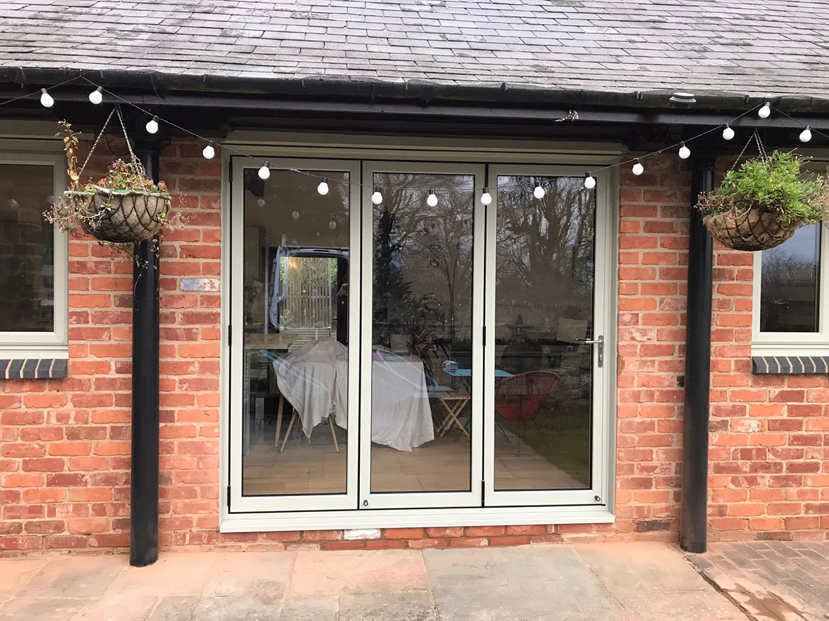 White bi-folding doors standing open onto a brick patio, with festoon lights strung across the elevation and a table laid inside.