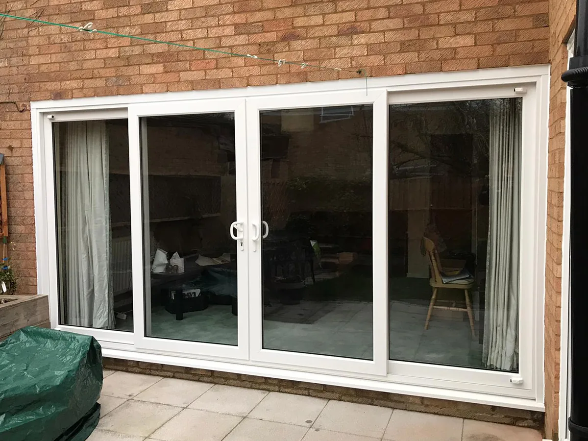 A white sliding patio door in the rear elevation of a brick house, curtains drawn back and the track visible along the threshold.